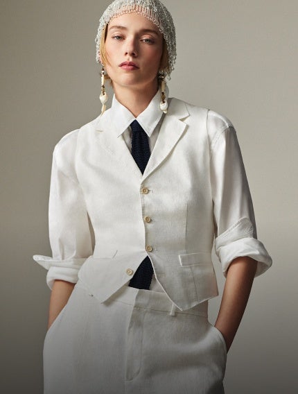 Woman wears white linen suit vest over white linen button-down shirt and white linen trousers.