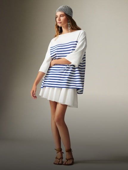 Woman wears oversized blue-and-white striped tee over white pleated skirt.
