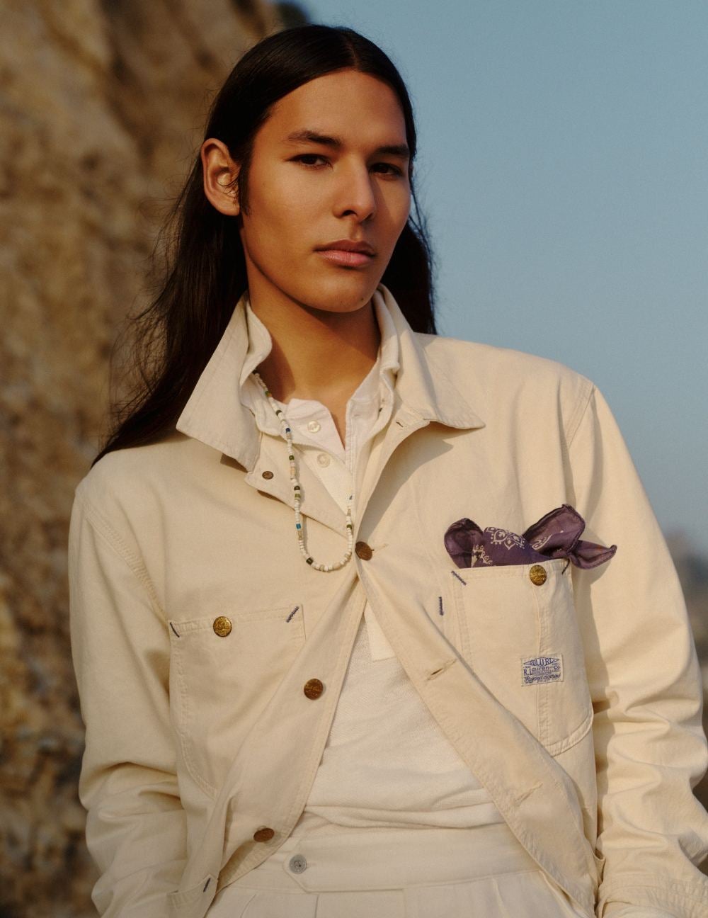 Man wears cream utility jacket over white outfit.