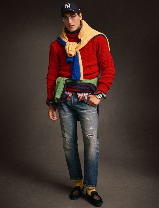 Man wears red cable-knit sweater and distressed jeans.
