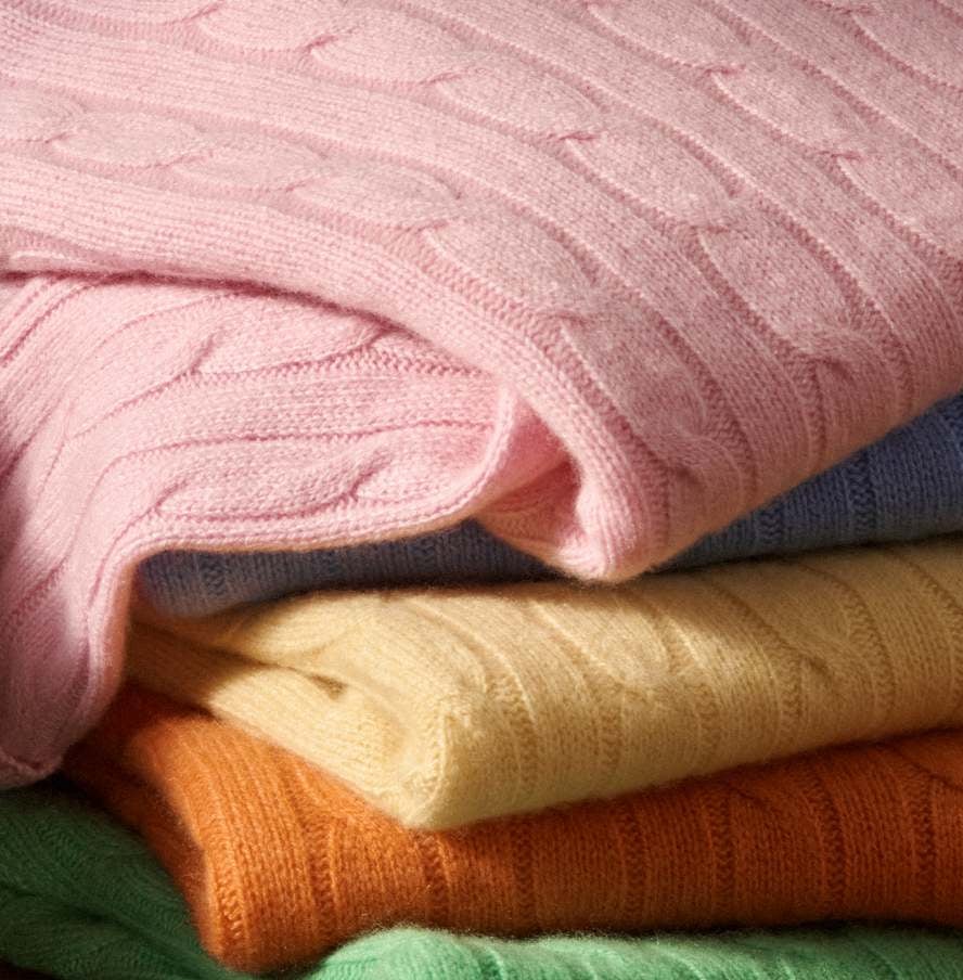 Close-up of pink, yellow, orange, and green cable-knit sweaters.