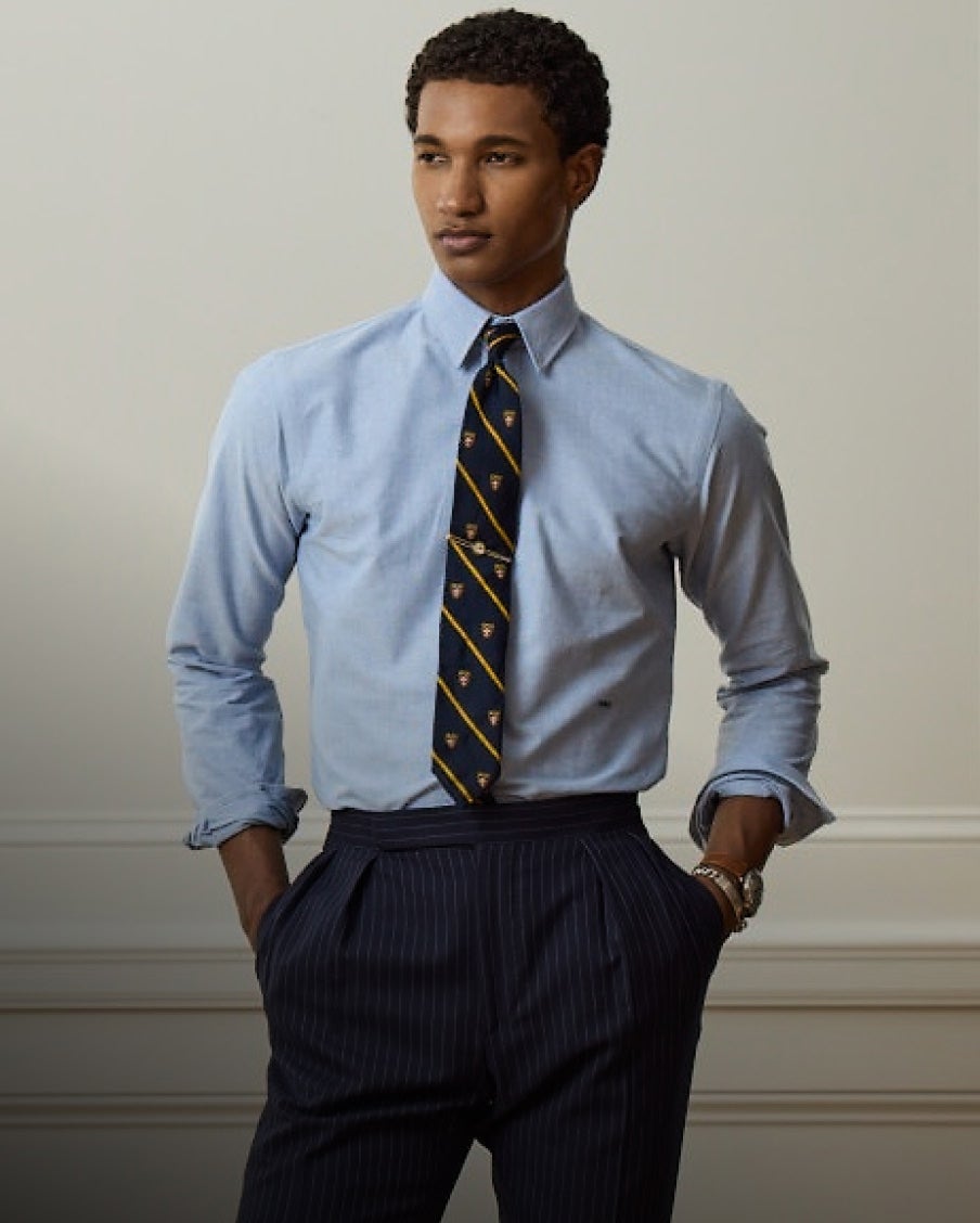 Man wears blue button-down shirt, tie, and navy pinstripe trousers.